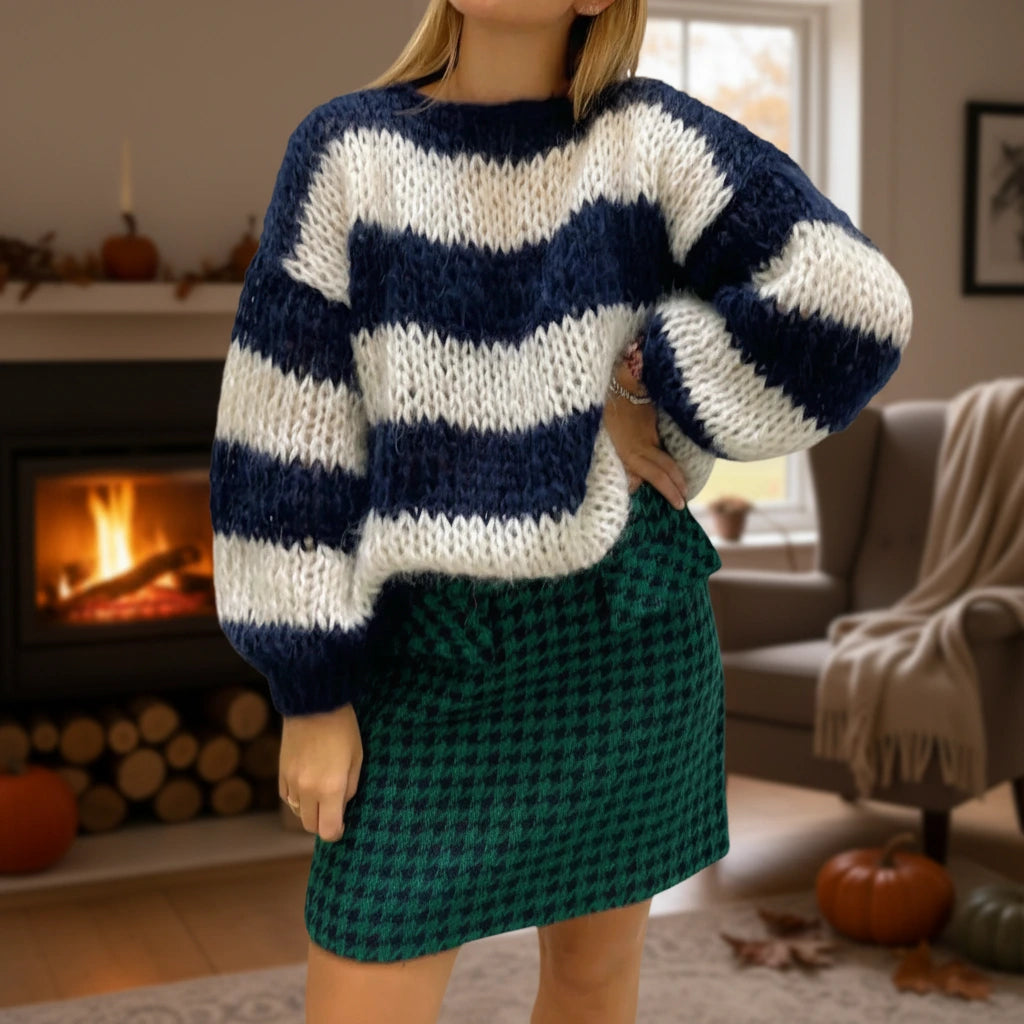 Woman wearing a navy blue striped chunky knit sweater by a fireplace, lifestyle shot
