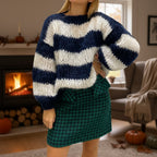 Woman wearing a navy blue striped chunky knit sweater by a fireplace, lifestyle shot