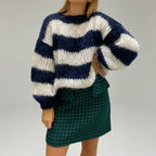 Woman wearing a navy blue and white striped chunky knit sweater with balloon sleeves, studio shot