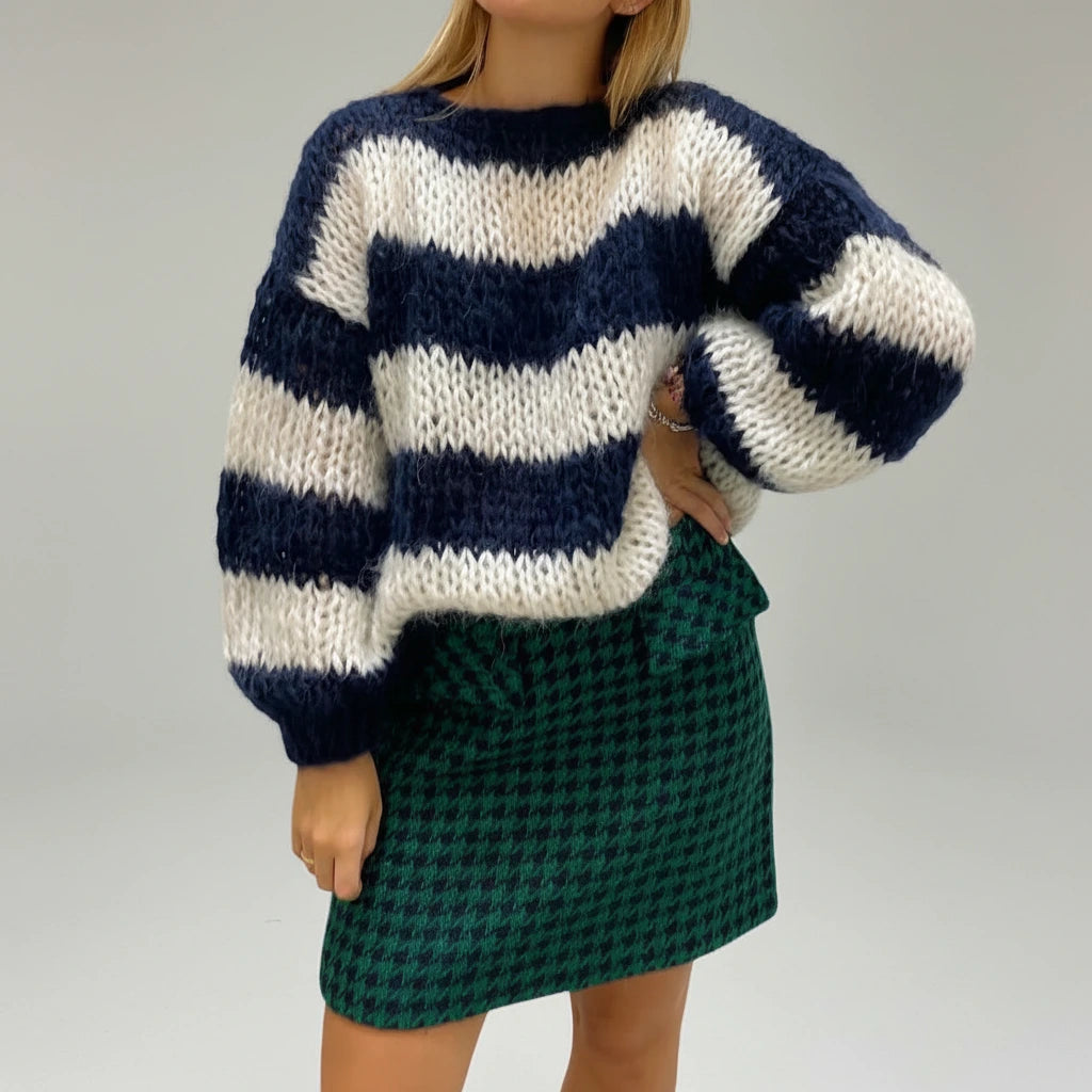 Woman wearing a navy blue and white striped chunky knit sweater with balloon sleeves, studio shot