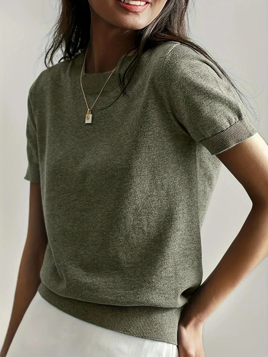 Woman wearing an olive green fine knit sweater with short sleeves and ribbed trim