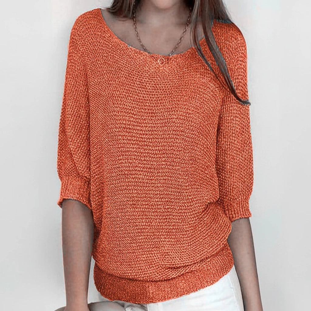 Woman wearing an orange relaxed knit sweater with wide neckline and dolman sleeves, studio shot