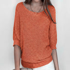 Woman wearing an orange relaxed knit sweater with wide neckline and dolman sleeves, studio shot