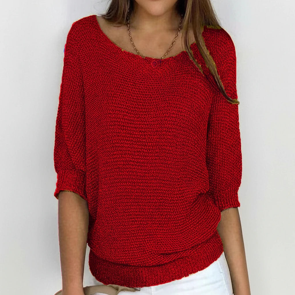 Woman wearing a red relaxed knit sweater with wide neckline and dolman sleeves, studio shot