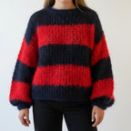 Woman wearing a red and black striped chunky knit sweater with balloon sleeves, studio shot