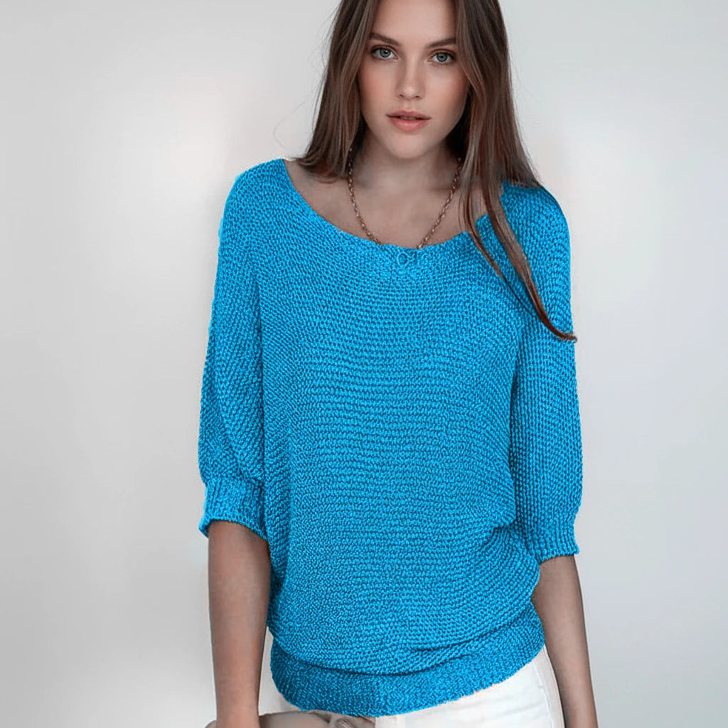 Woman wearing a sky blue relaxed knit sweater with wide neckline and dolman sleeves, studio shot