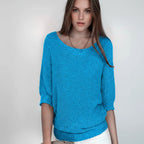 Woman wearing a sky blue relaxed knit sweater with wide neckline and dolman sleeves, studio shot
