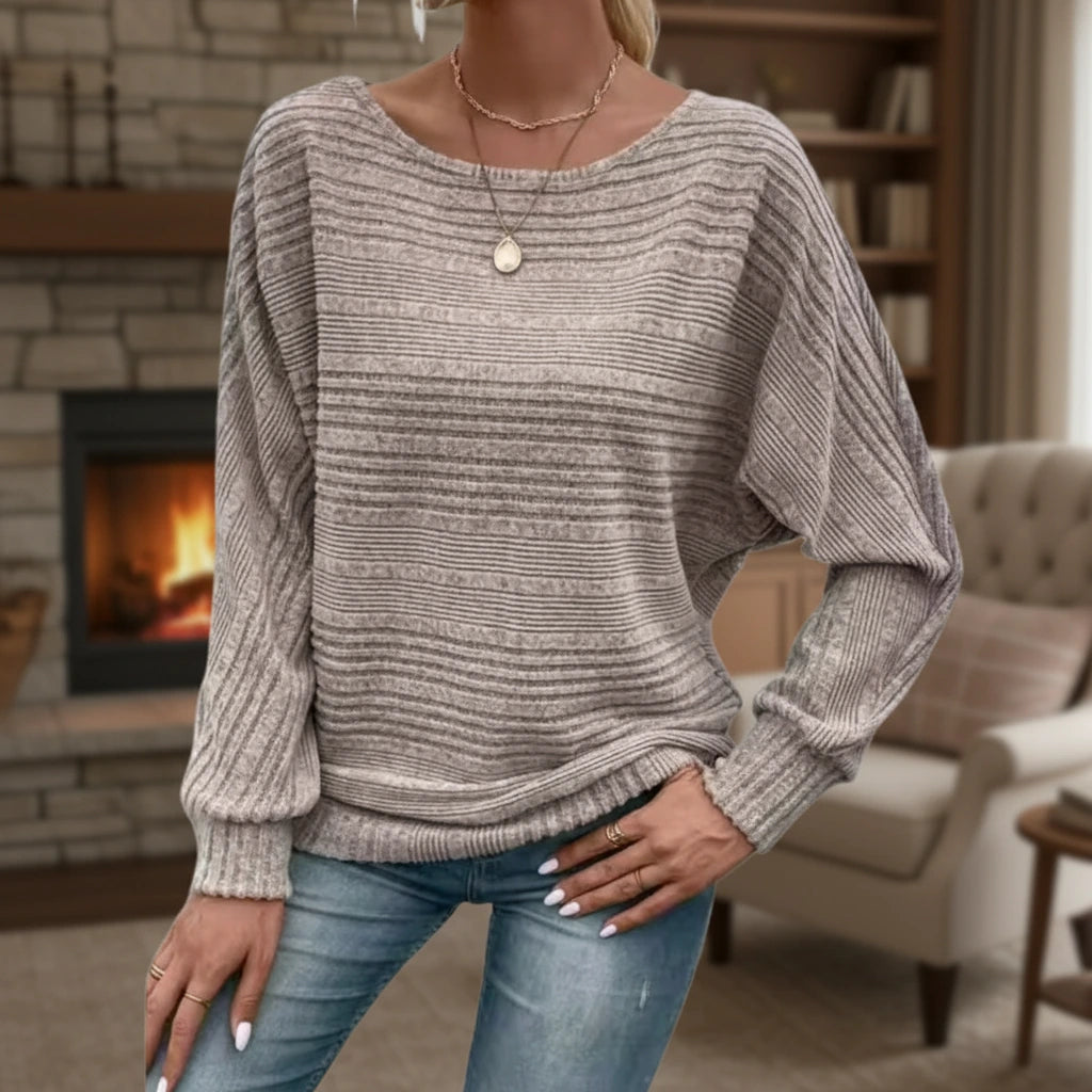 Woman wearing taupe textured knit sweater with batwing sleeves by a fireplace