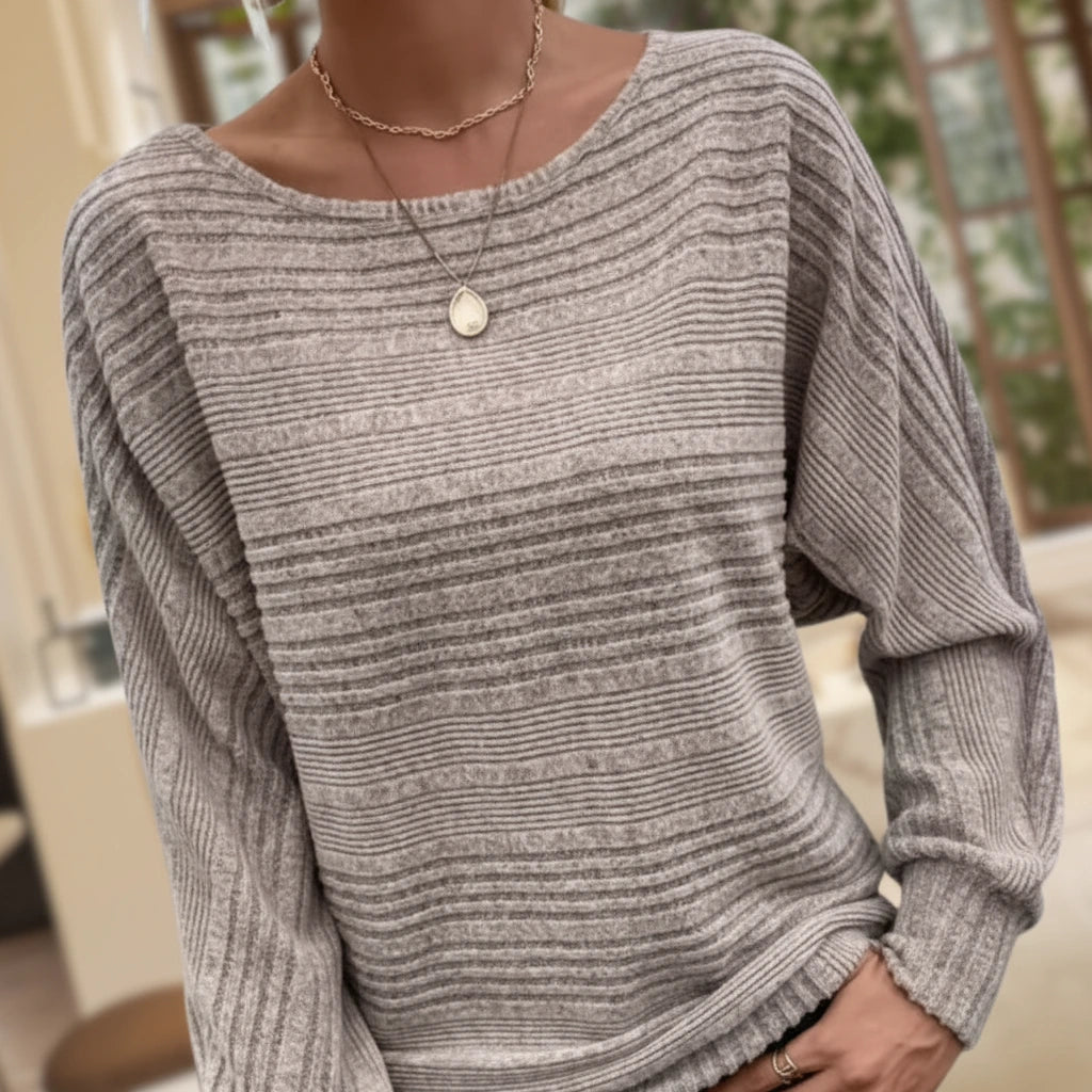 Woman wearing taupe textured knit sweater with batwing sleeves, near a window