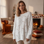 Woman wearing a white oversized open knit sweater by a fireplace, lifestyle shot