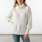 Woman wearing white ribbed cowl neck sweater with button cuffs, studio photo