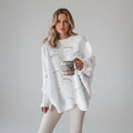 Woman wearing a white oversized open knit sweater with draped asymmetric hem, studio shot