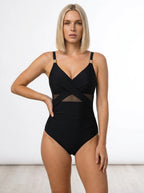 Woman wearing a black shaping one-piece swimsuit with crossed straps and mesh cutout accents in a studio setting