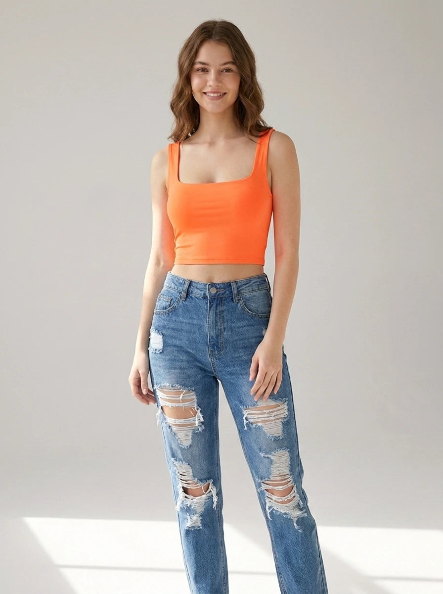 Driftly women's orange polyester cropped tank top with a slash neckline, styled with ripped denim jeans in a minimalist studio setting.