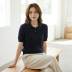 Driftly women's navy cotton polo t-shirt, styled with beige linen trousers, seated in a bright interior.