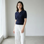 Driftly women's navy cotton polo t-shirt, styled with white wide-leg trousers in a minimalist studio setting.