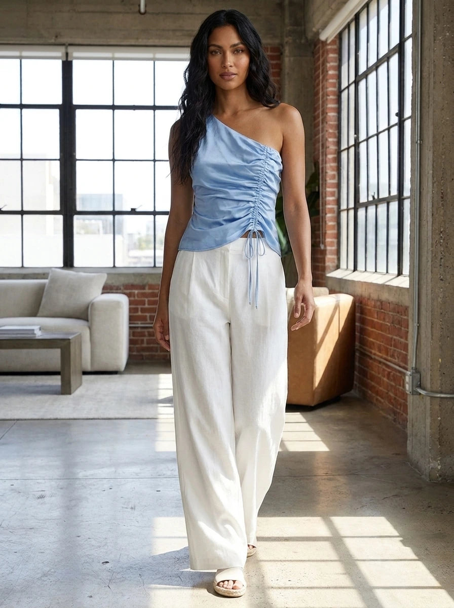 Woman wearing a blue satin one-shoulder ruched top in a bright loft interior
