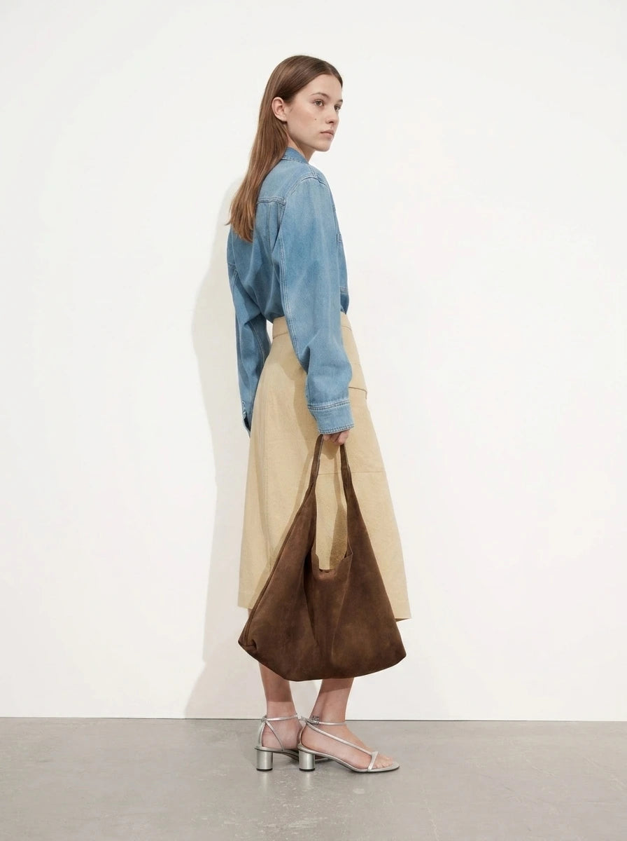 Woman carrying a brown suede slouchy shoulder tote bag, side view in a studio setting