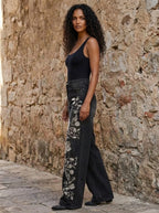 Woman in black floral print wide-leg trousers, different angle against a stone wall
