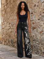 Woman wearing black wide-leg trousers with a white floral print against a stone wall