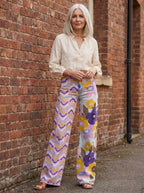 Woman wearing purple bohemian floral print wide-leg trousers, different pose against a brick wall