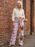 Woman wearing purple bohemian floral print wide-leg trousers against a brick wall