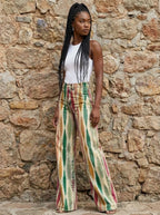 Woman in multicolor striped bohemian wide-leg trousers, different angle against a stone wall