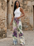 Woman in purple floral print wide-leg trousers standing in a stone courtyard