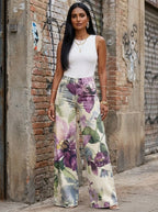 Woman in purple floral print wide-leg trousers standing against an urban wall