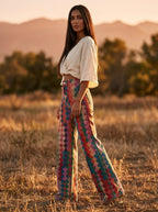 Woman wearing multicolor bohemian chic high-waisted wide-leg trousers, outdoor golden hour field setting