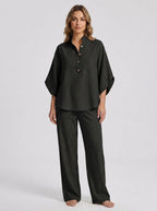 Woman wearing a black linen-style two-piece set, relaxed button-front top and wide-leg trousers, studio shot