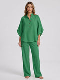 Woman wearing a green linen-style two-piece set, relaxed button-front top and wide-leg trousers, studio shot