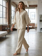 Woman wearing a sand beige linen-style two-piece set indoors, relaxed fit blouse and flowing trousers