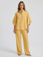 Woman wearing a yellow linen-style two-piece set, relaxed button-front top and wide-leg trousers, studio shot