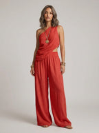 Woman wearing a red one-shoulder ruched cutout cami top and wide-leg pants two-piece set in a studio setting