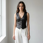 Driftly women's black faux leather V-neck vest, styled with white wide-leg trousers in a minimalist studio setting.