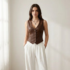 Driftly women's brown faux leather V-neck vest, styled with white wide-leg trousers in a minimalist studio setting.