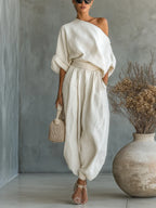 Woman wearing an off-white off-shoulder two-piece outfit with wide-leg pants, studio setting