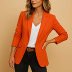 Woman wearing an orange one-button fitted blazer in a studio setting