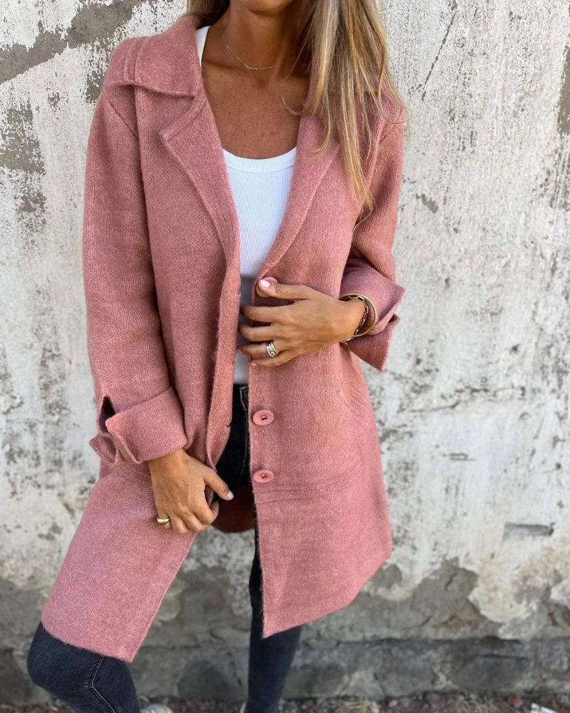 Woman wearing a dusty pink button-up long cardigan coat against a textured concrete wall