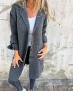 Woman wearing a grey button-up long cardigan coat against a textured concrete wall