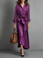 Woman wearing a purple bow-belted maxi shirt dress with a tote bag, studio setting