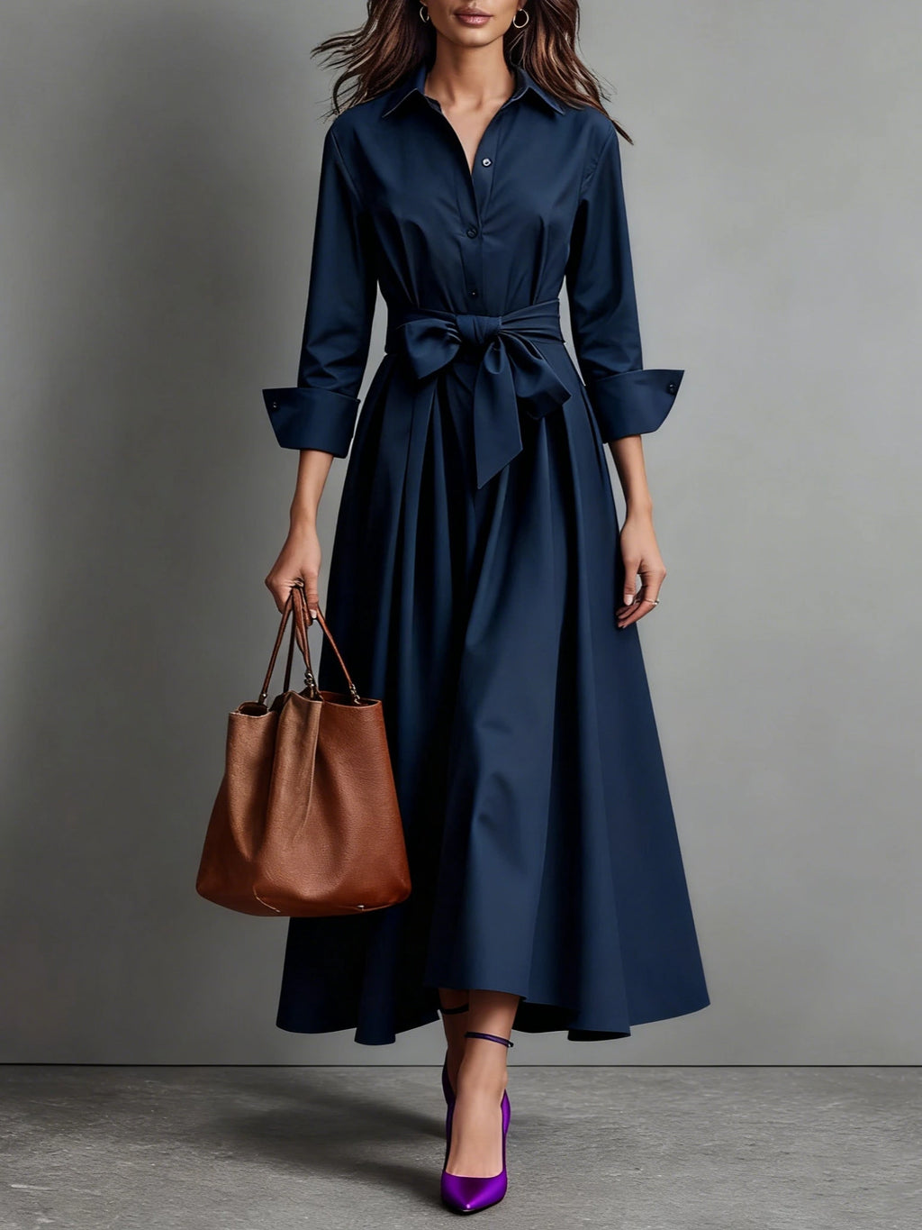 Woman wearing a navy blue bow-belted maxi shirt dress with a tote bag, studio setting