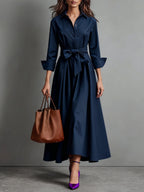 Woman wearing a navy blue bow-belted maxi shirt dress with a tote bag, studio setting