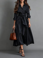 Woman wearing a black bow-belted maxi shirt dress with a tote bag, studio setting