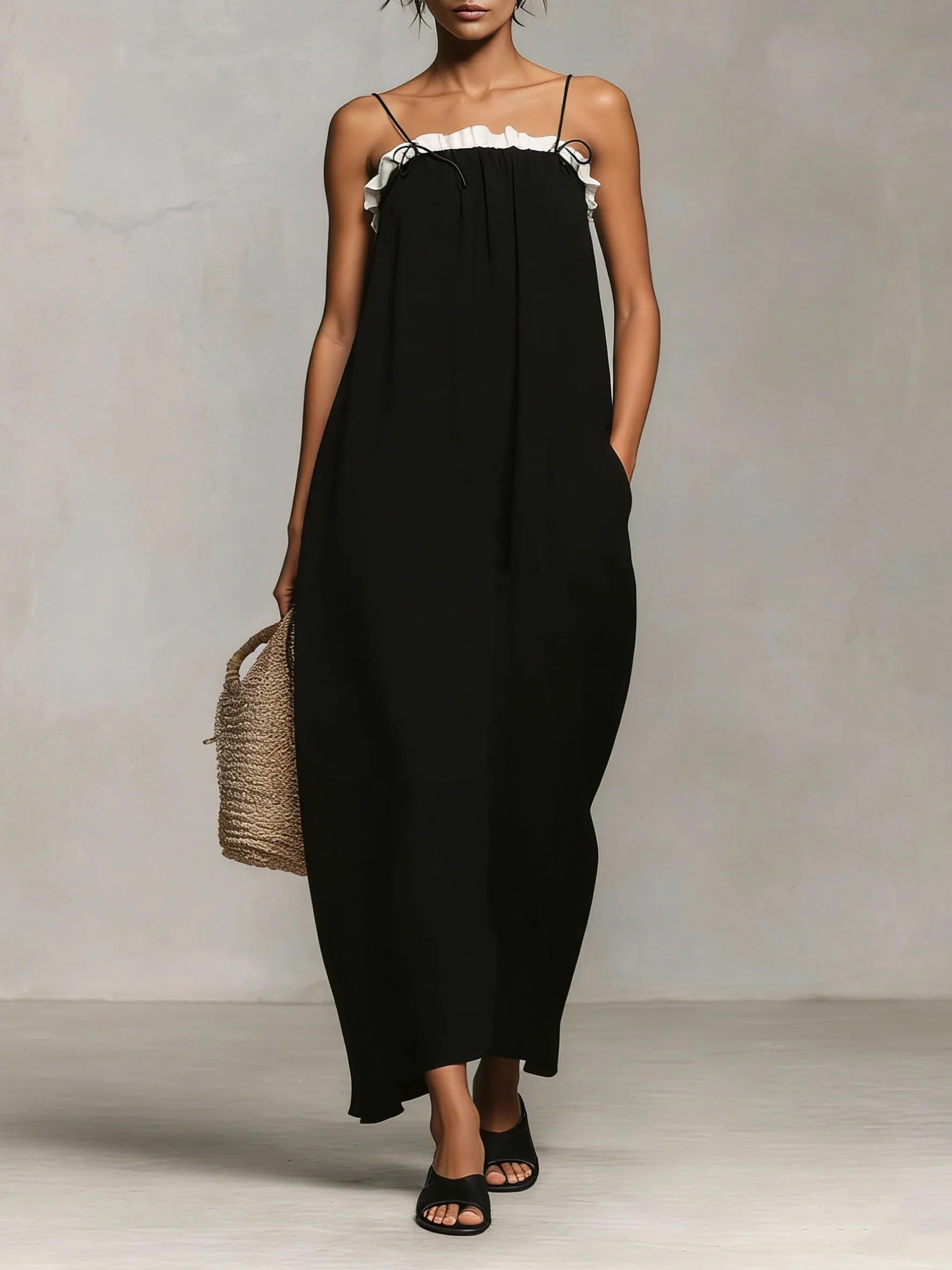 Woman wearing a black spaghetti strap maxi dress with a white ruffle trim, front view