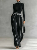 Woman wearing a black turtleneck and black wide-leg trousers with white contrast piping, studio setting