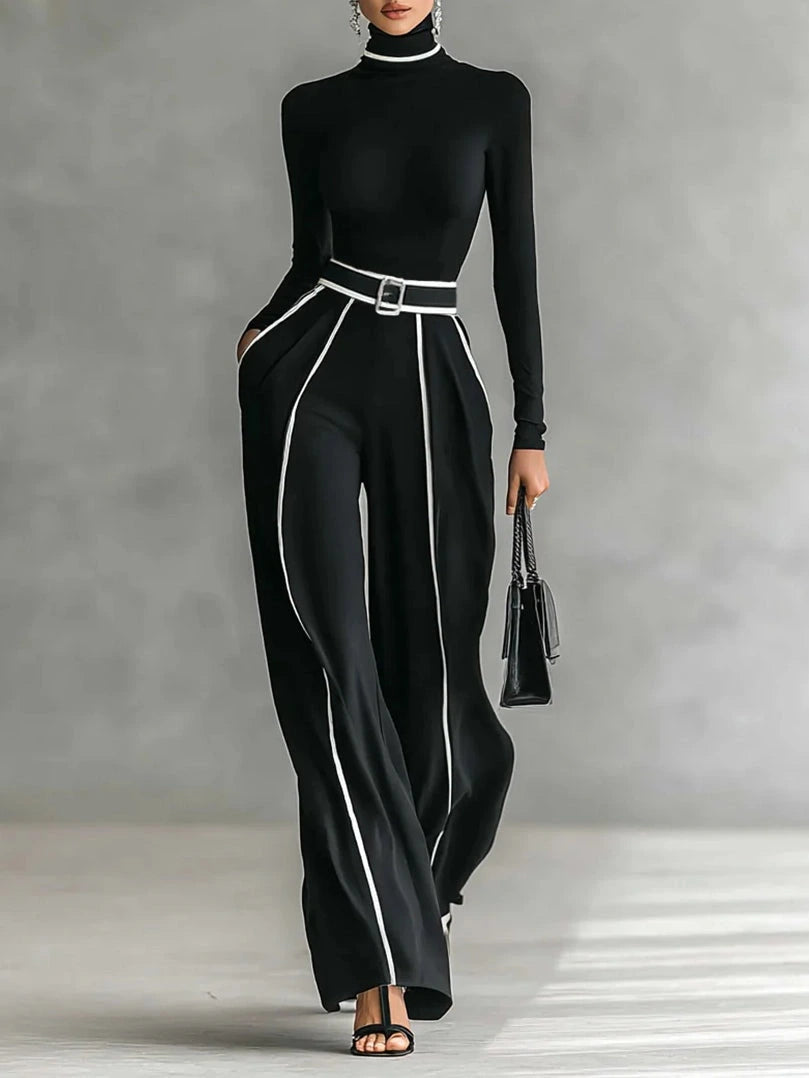 Woman wearing a black turtleneck and black wide-leg trousers with white contrast piping, studio setting