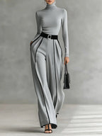 Woman wearing a gray turtleneck and gray wide-leg trousers with white contrast piping, studio setting
