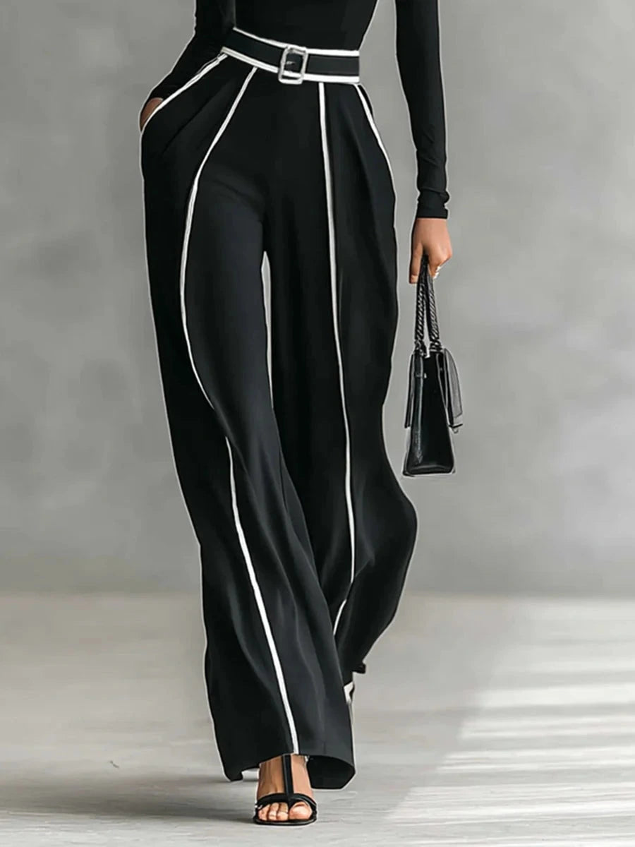 Woman wearing a black turtleneck and black wide-leg trousers with white contrast piping, side view